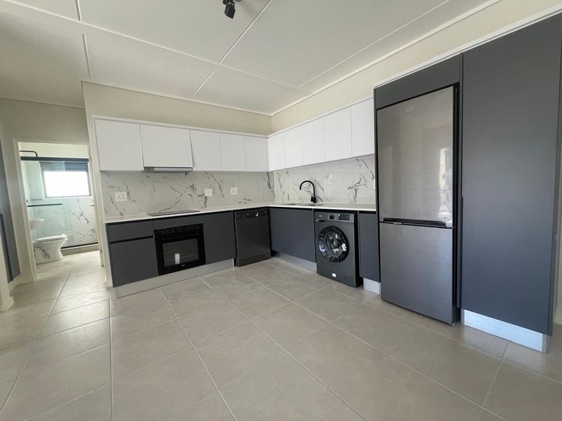 Modern kitchen featuring sleek two-tone cabinetry, marble-look splashback, integrated appliances, and tiled flooring, with an adjacent view into the bathroom.
