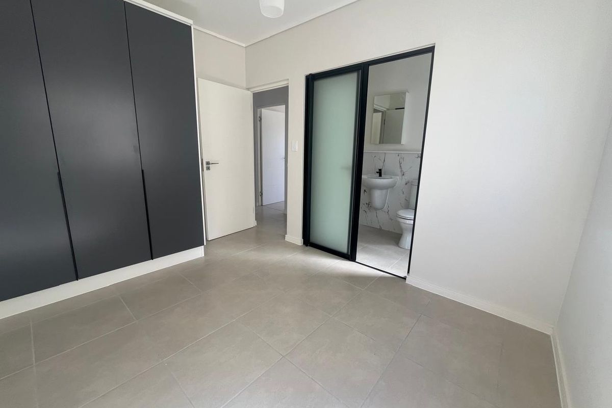 Modern bedroom featuring sleek dark built-in cupboards, neutral tiled flooring, and direct access to an en-suite bathroom through a contemporary sliding door.