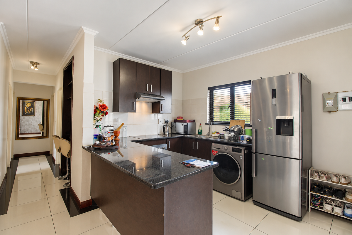A functional kitchen featuring dark wood cabinetry, granite countertops, a tiled backsplash, and integrated stainless steel sink, complemented by modern tiled flooring.