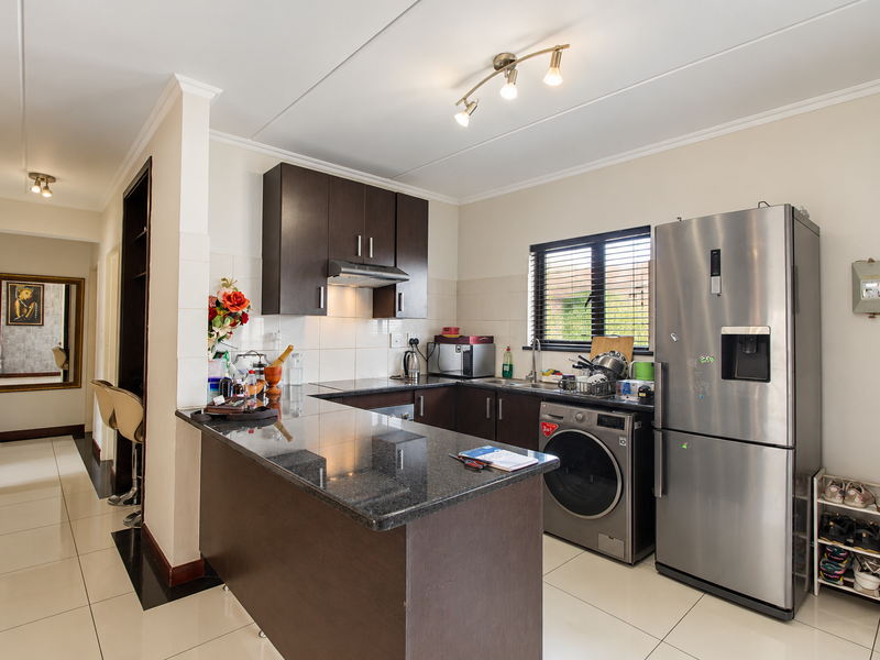 A functional kitchen featuring dark wood cabinetry, granite countertops, a tiled backsplash, and integrated stainless steel sink, complemented by modern tiled flooring.