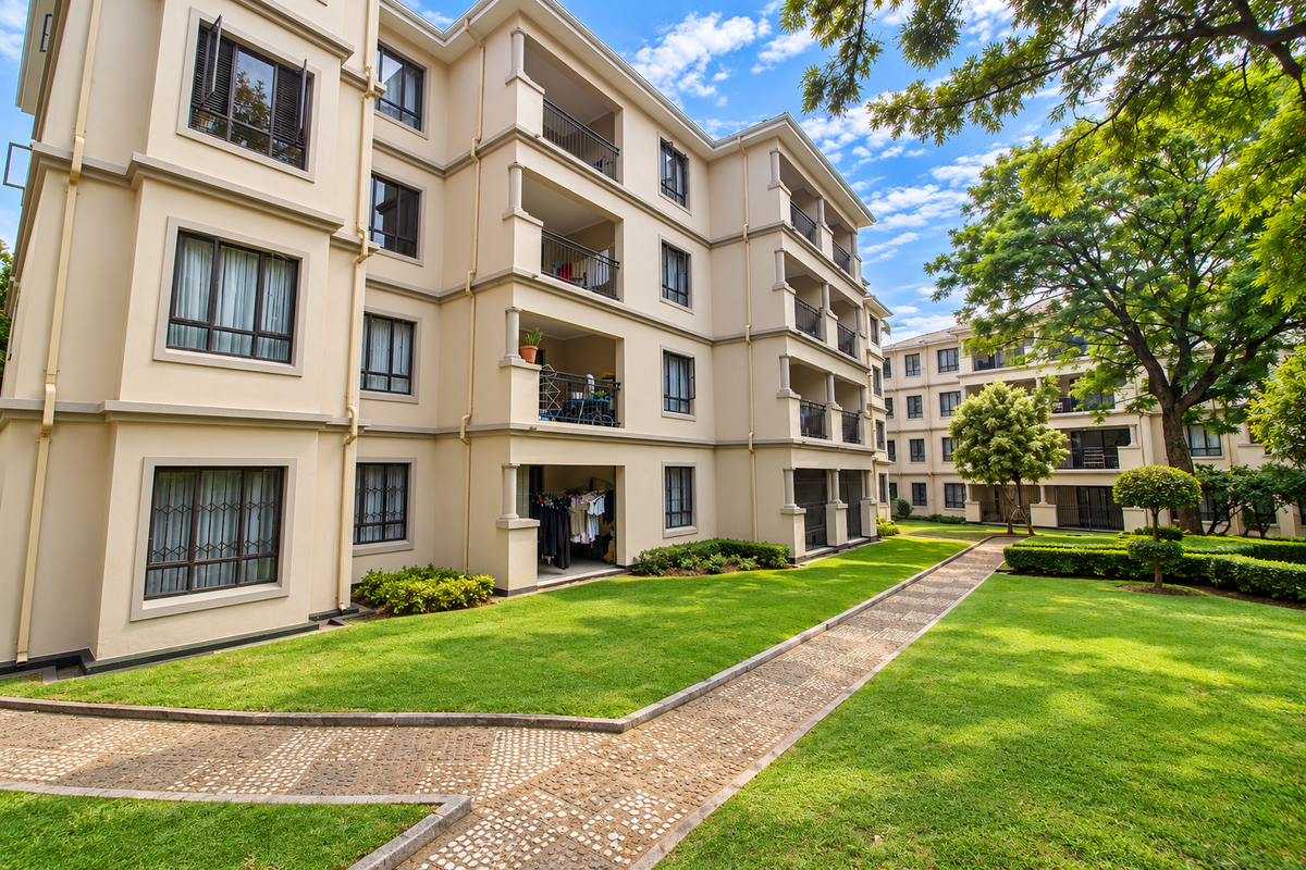 A well-maintained apartment complex exterior featuring landscaped gardens, paved walkways, and private balconies with security bars on lower-level windows.