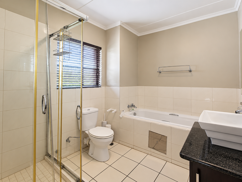 A clean, functional bathroom featuring a glass-enclosed shower, a built-in bathtub, a toilet, and a vanity with a granite countertop.