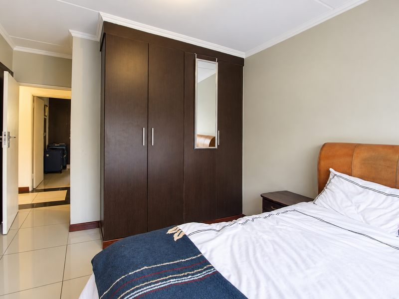 A bedroom featuring a dark wood built-in wardrobe with a central mirror, tiled flooring, and neutral wall finishes.