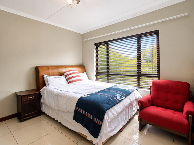 A well-maintained bedroom featuring neutral wall tones, large windows with venetian blinds, and polished tile flooring.