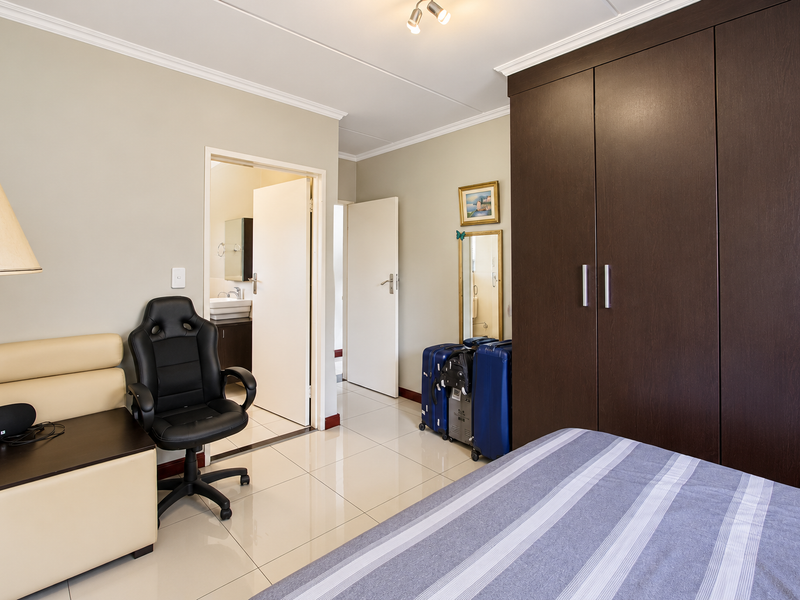 A well-maintained bedroom featuring tiled flooring, crown molding, and a large dark wood built-in wardrobe with direct access to an en-suite bathroom.