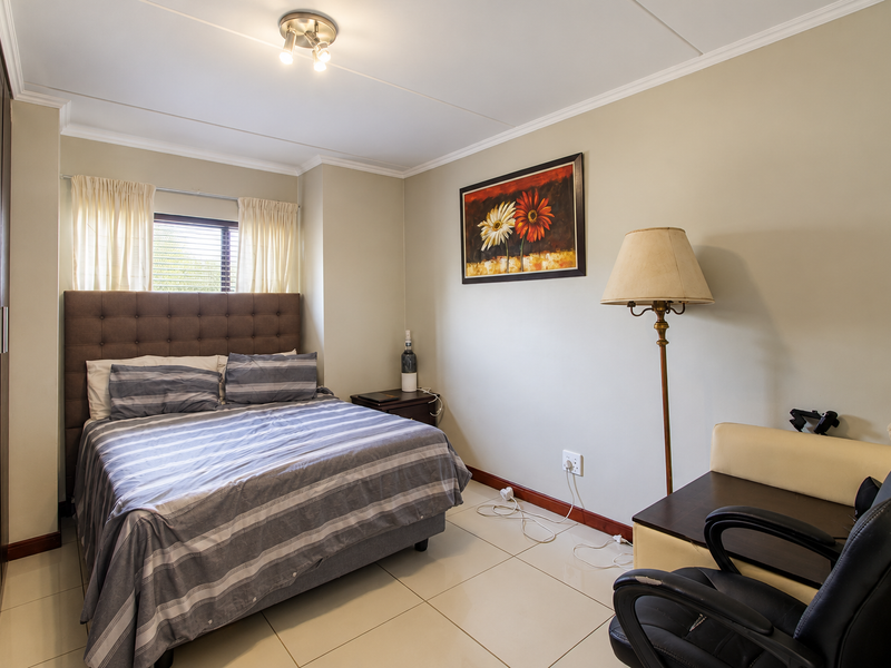 A well-maintained bedroom featuring tiled flooring, a built-in wardrobe, and neutral wall finishes, providing a clean and functional living space.
