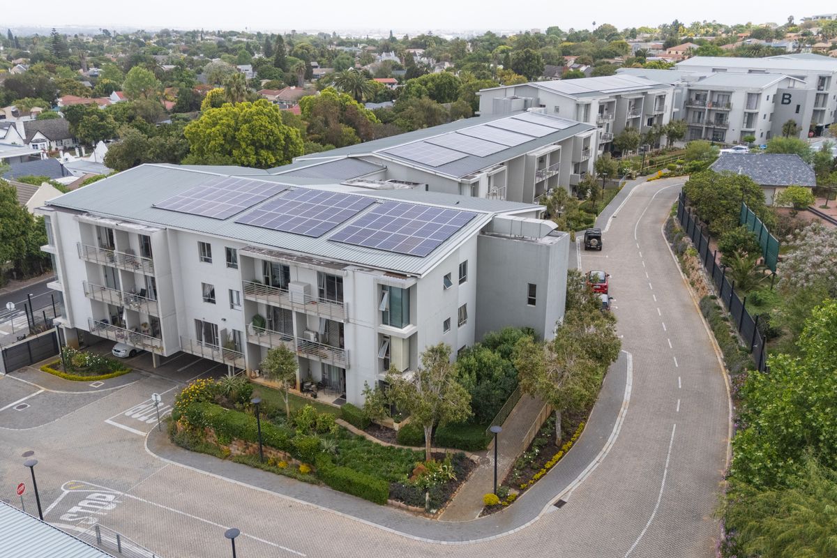 Aerial view of a modern apartment complex featuring solar panels on the roof, private balconies, and well-maintained landscaped grounds with paved access roads.