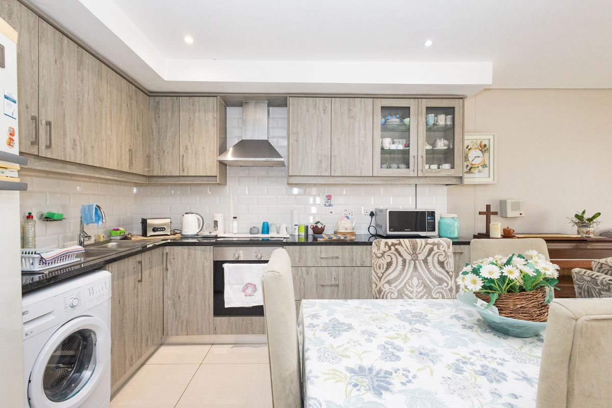 A well-maintained kitchen featuring wood-look laminate cabinetry, subway tile backsplash, built-in oven, hob, extractor fan, and an integrated washing machine.