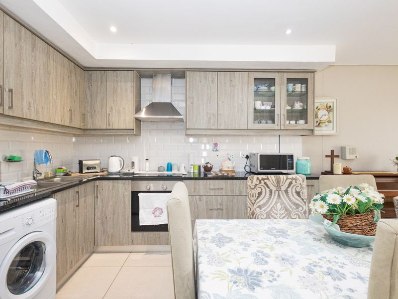 A well-maintained kitchen featuring wood-look laminate cabinetry, subway tile backsplash, built-in oven, hob, extractor fan, and an integrated washing machine.