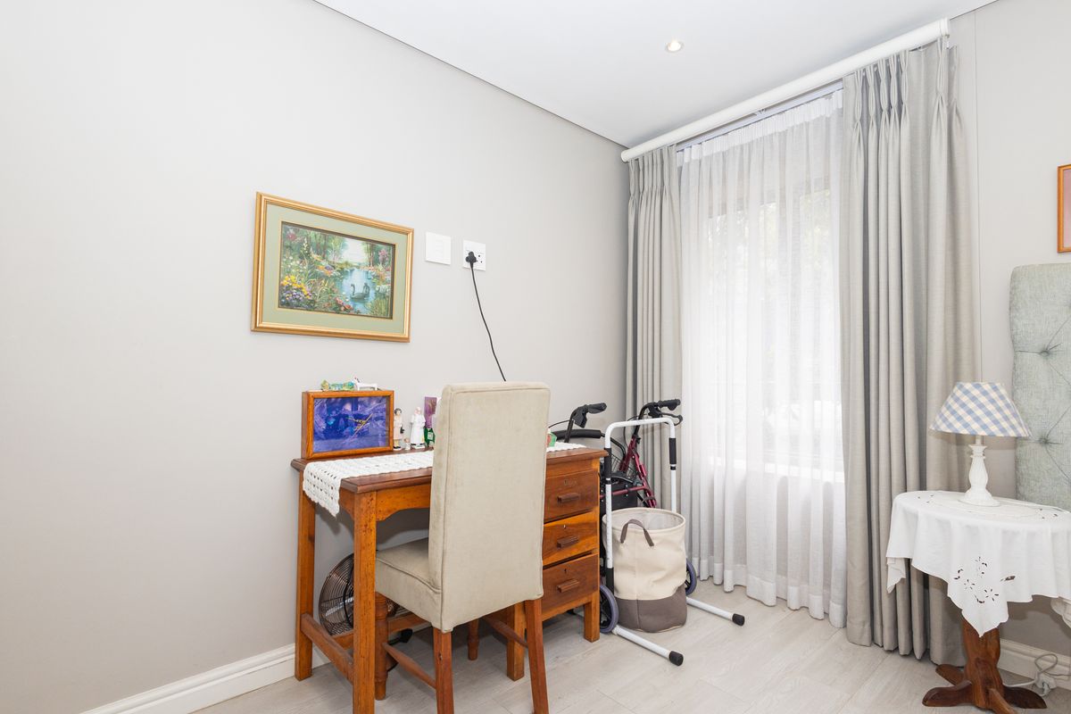 A well-maintained bedroom featuring neutral wall tones, laminate flooring, and floor-to-ceiling curtains providing natural light.