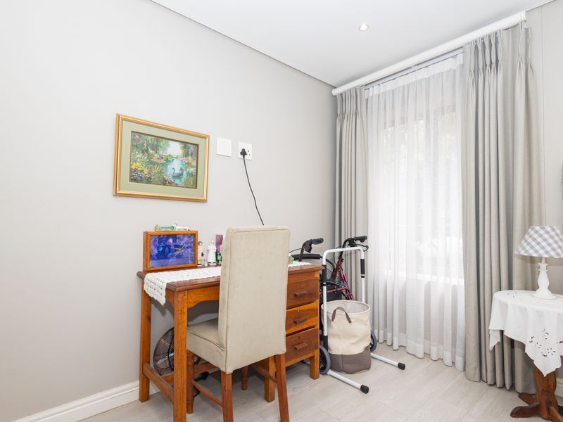 A well-maintained bedroom featuring neutral wall tones, laminate flooring, and floor-to-ceiling curtains providing natural light.