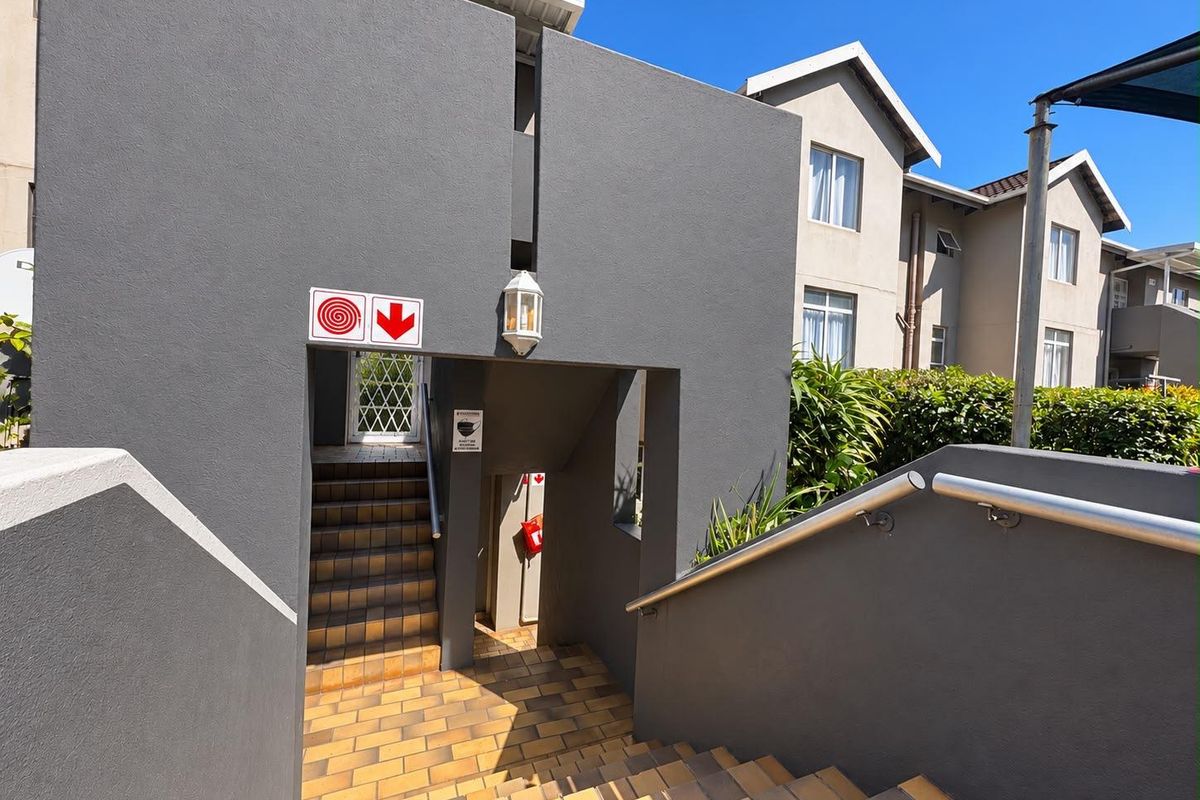 An exterior view of a modern apartment complex featuring a tiled staircase with metal handrails and grey painted walls.
