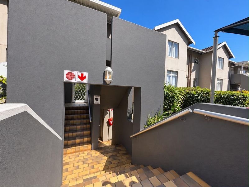 An exterior view of a modern apartment complex featuring a tiled staircase with metal handrails and grey painted walls.