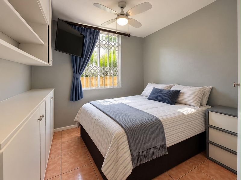 A well-maintained bedroom featuring built-in storage cabinetry, a ceiling fan, and tiled flooring, with security bars installed on the window.
