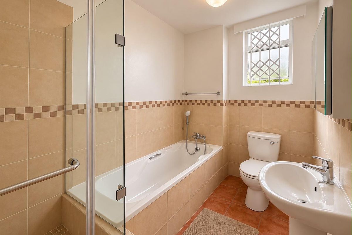 A clean, functional bathroom featuring a glass-enclosed shower, a bathtub, a pedestal basin, and a toilet with neutral wall and floor tiling.