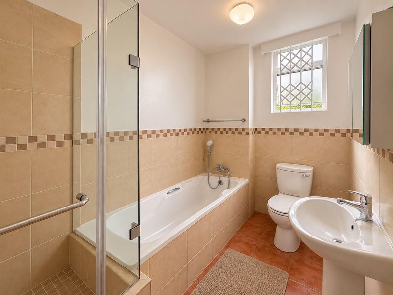 A clean, functional bathroom featuring a glass-enclosed shower, a bathtub, a pedestal basin, and a toilet with neutral wall and floor tiling.