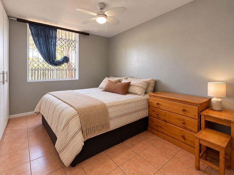 A well-maintained bedroom featuring tiled flooring, a ceiling fan, and a built-in wardrobe with a security gate on the window.
