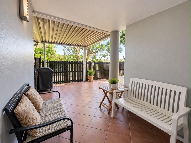 A covered outdoor patio area featuring tiled flooring, a support column, and a timber picket fence, providing a functional space for outdoor relaxation.