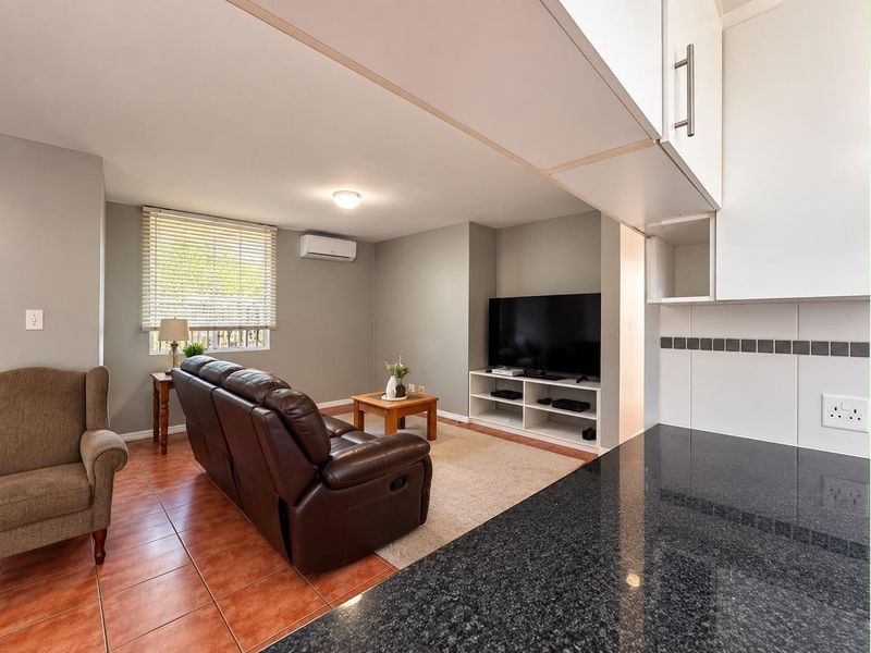 Open-plan living area featuring tiled flooring, a modern kitchen with granite countertops, and a wall-mounted air conditioning unit.