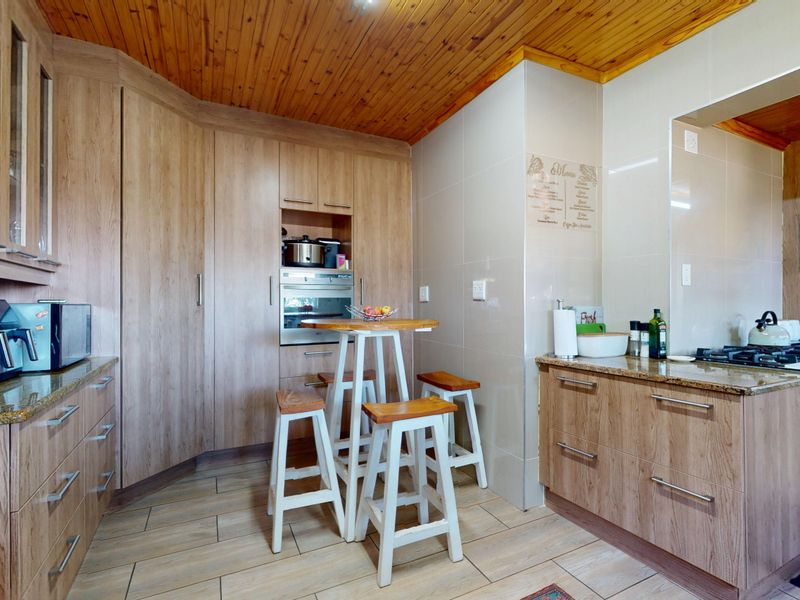A functional kitchen featuring wood-look cabinetry, granite countertops, a built-in oven, gas hob, and a distinctive timber-clad ceiling.