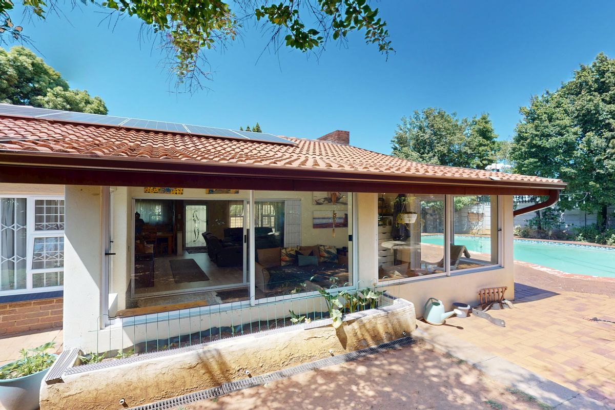 Rear view of the house featuring a terracotta tiled roof with solar panels, a paved patio area, and a swimming pool.