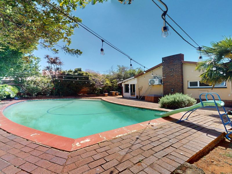 Outdoor pool area featuring brick paving, a built-in brick chimney, and a pool slide, set within a mature garden environment.