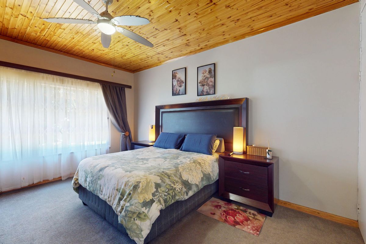 A comfortable bedroom featuring a distinctive timber tongue and groove ceiling, ceiling fan, and built-in storage cupboards.