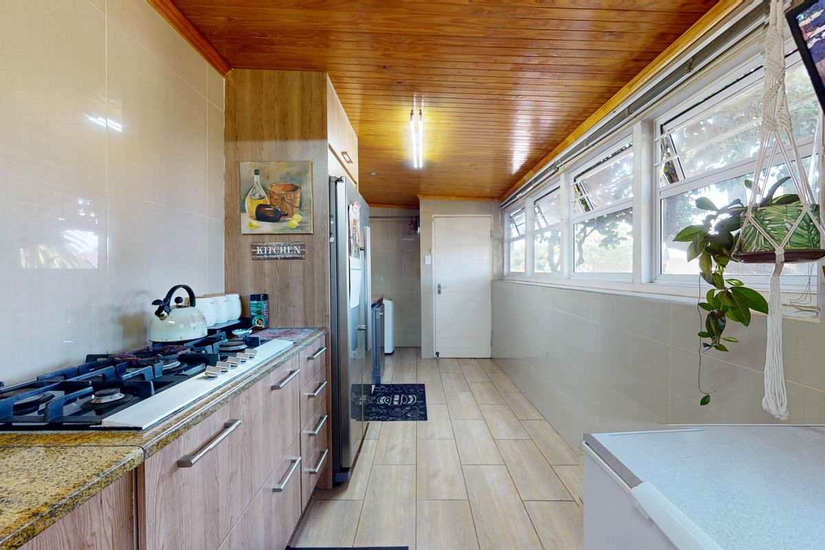 A functional kitchen featuring a gas hob, granite countertops, wood-paneled ceiling, and tiled flooring with ample natural light from a row of windows.