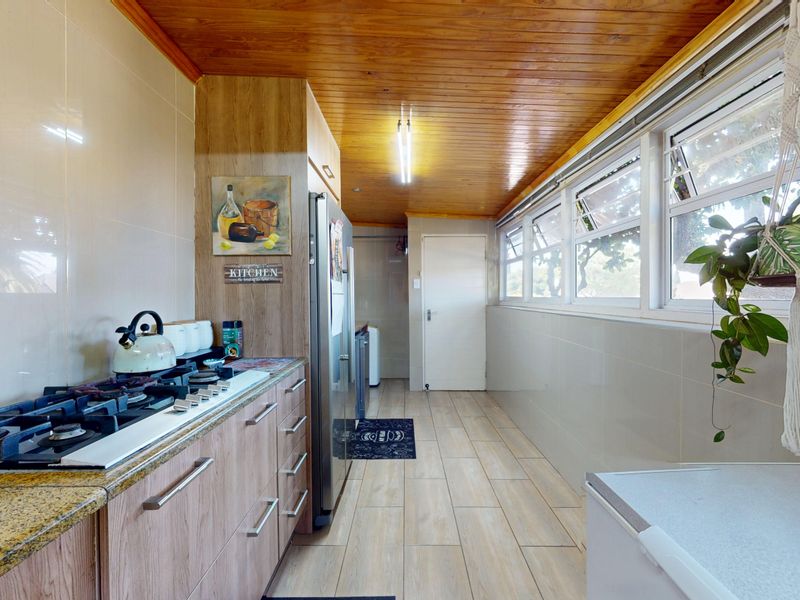 A functional kitchen featuring a gas hob, granite countertops, wood-paneled ceiling, and tiled flooring with ample natural light from a row of windows.