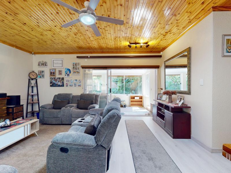 Spacious living room featuring a warm timber-paneled ceiling, ceiling fan, split-system air conditioning, and large sliding glass doors providing access to the patio area.