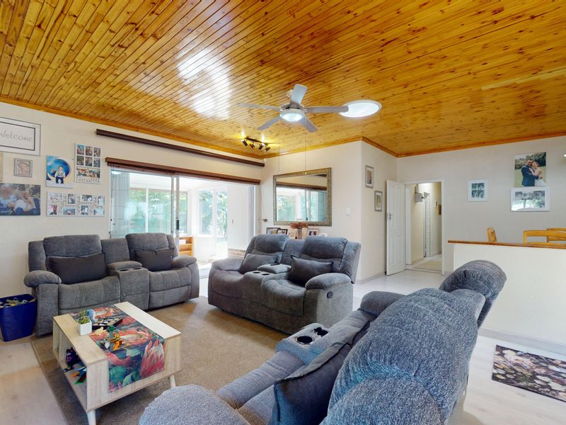 Spacious living room featuring a warm timber tongue and groove ceiling, ceiling fan, and large sliding glass doors providing access to the outdoor area.