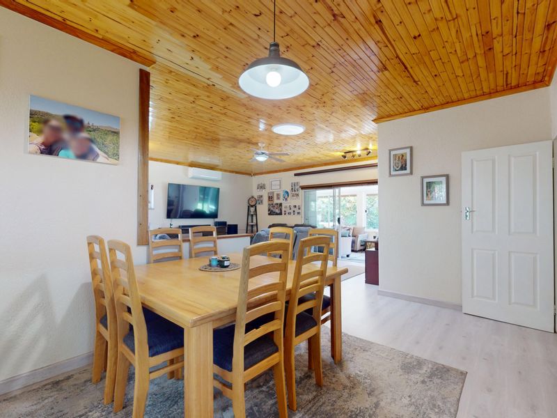 Open-plan dining and living area featuring a warm timber tongue and groove ceiling, laminate flooring, and direct access to the outdoor space.