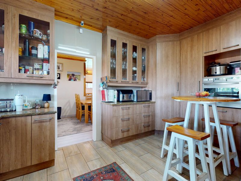 A functional kitchen featuring wood-look cabinetry, granite countertops, a built-in oven, and a distinctive timber-paneled ceiling with tiled flooring throughout.