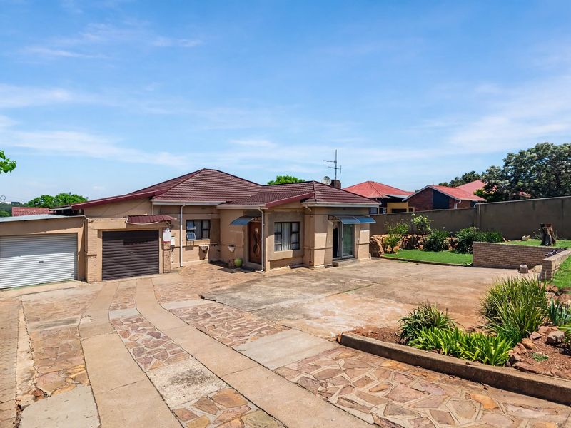 Front view of a single-story house featuring a tiled roof, attached garage, and a paved driveway with established garden borders.
