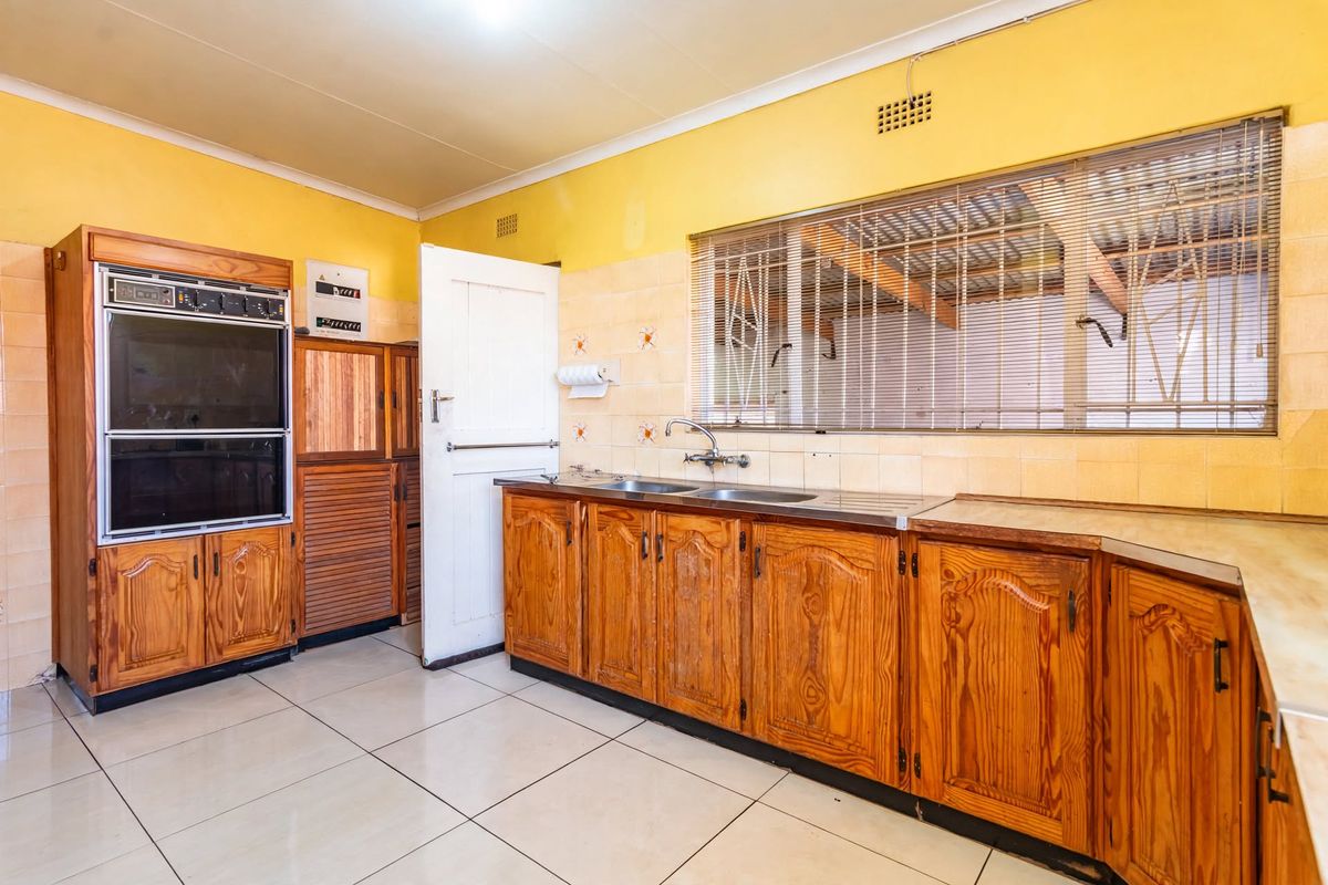A functional kitchen featuring traditional wooden cabinetry, built-in eye-level oven, double sink, and tiled splashbacks, offering a classic layout with potential for modernization.
