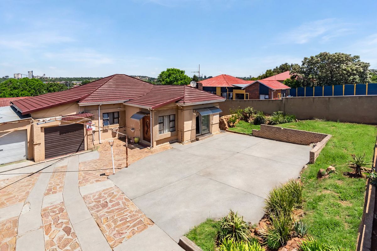Aerial view of a residential property featuring a tiled roof, concrete driveway, stone paving, and a private garden area with boundary walls.