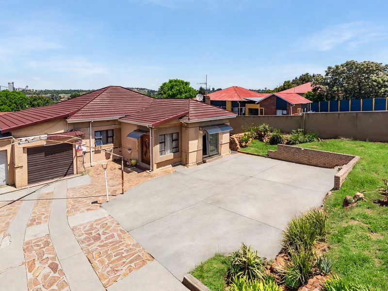 Aerial view of a residential property featuring a tiled roof, concrete driveway, stone paving, and a private garden area with boundary walls.