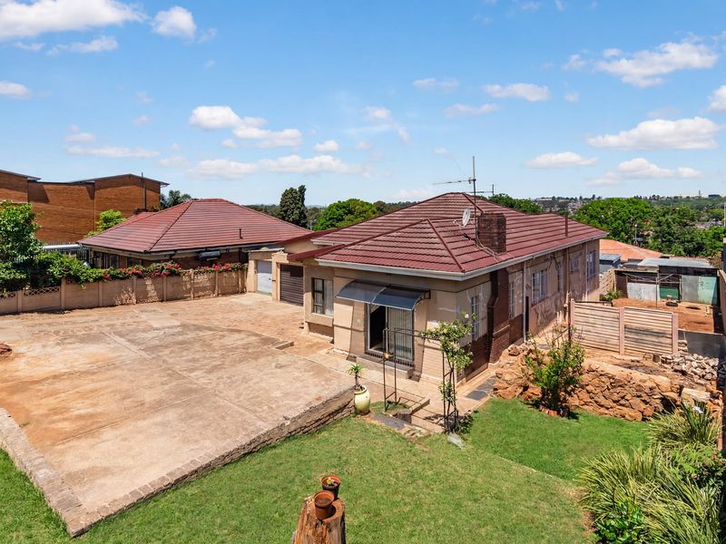 Aerial view of the property showing the rear yard, concrete driveway, lawn, and tiled roof structure.
