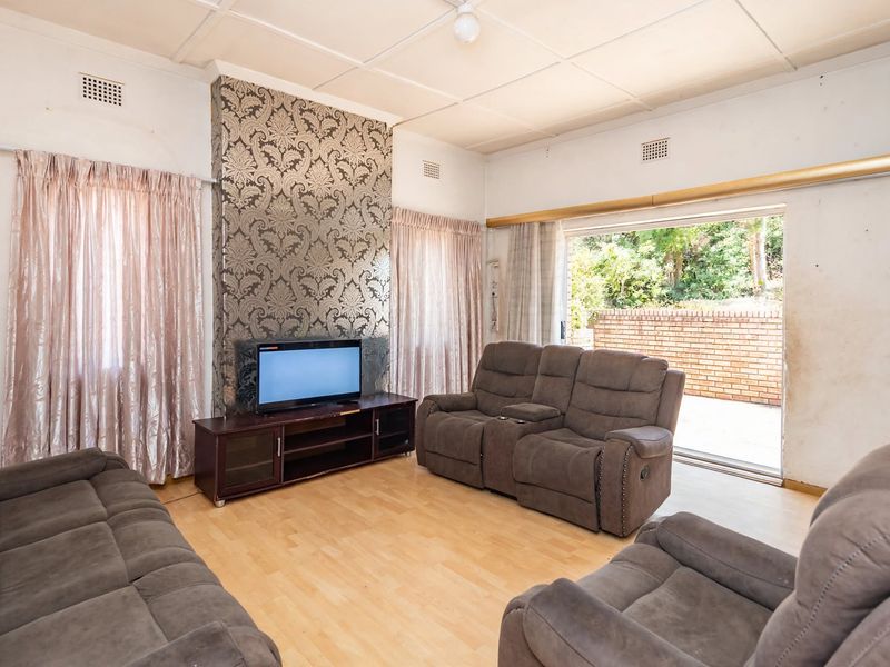 A living room featuring laminate flooring, a decorative feature wall, and a sliding glass door providing access to the outdoor patio area.