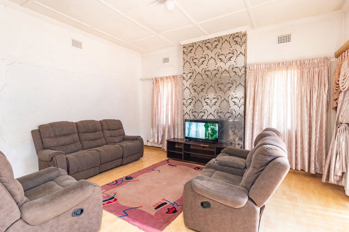 A living room featuring a decorative feature wall, tiled ceiling, and visible wall cracks requiring maintenance.
