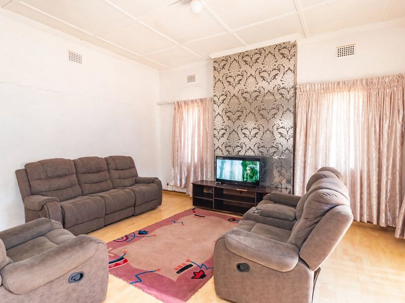 A living room featuring a decorative feature wall, tiled ceiling, and visible wall cracks requiring maintenance.