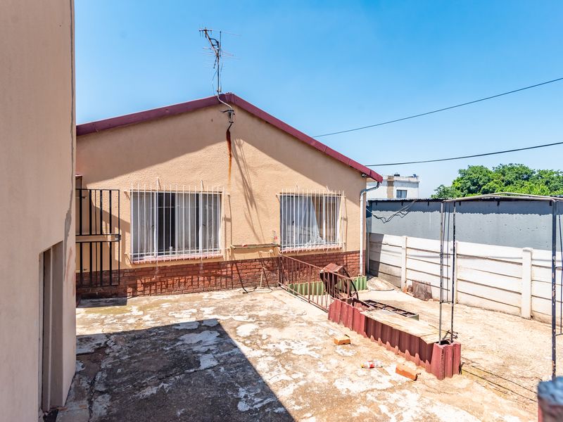 Rear exterior view of the property featuring a concrete patio area, security bars on windows, and a perimeter boundary wall.