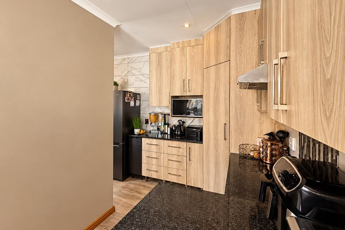Modern kitchen featuring light-wood cabinetry, dark granite countertops, built-in microwave, and a stylish tiled backsplash.