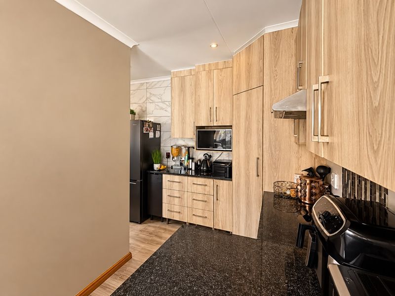 Modern kitchen featuring light-wood cabinetry, dark granite countertops, built-in microwave, and a stylish tiled backsplash.