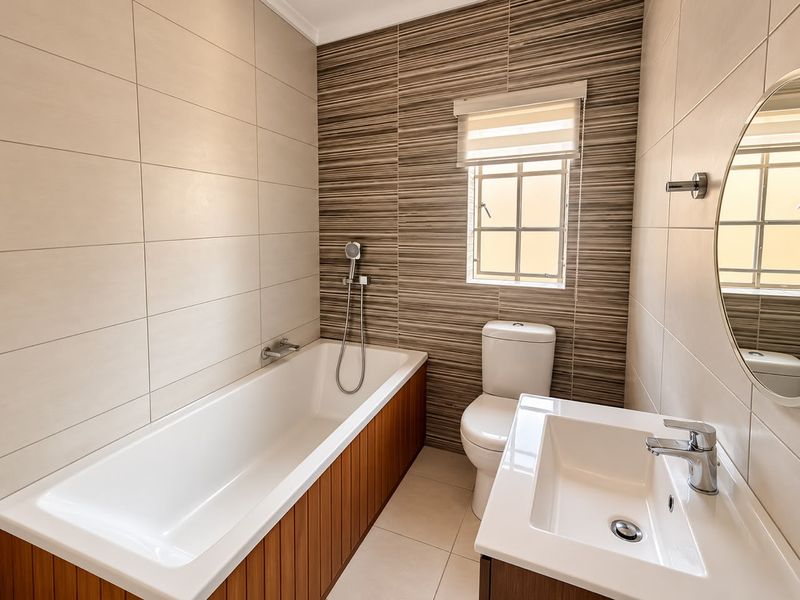 Modern bathroom featuring a built-in bathtub with wood-panel finish, a vanity basin, and a toilet, complemented by neutral and textured wall tiling.