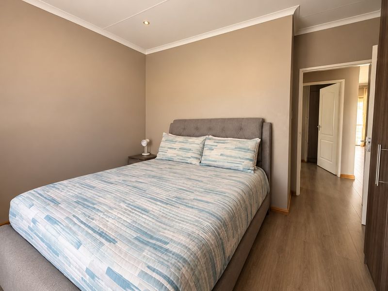 A well-maintained bedroom featuring laminate flooring, recessed downlighting, and neutral wall tones, providing a clean and comfortable living space.