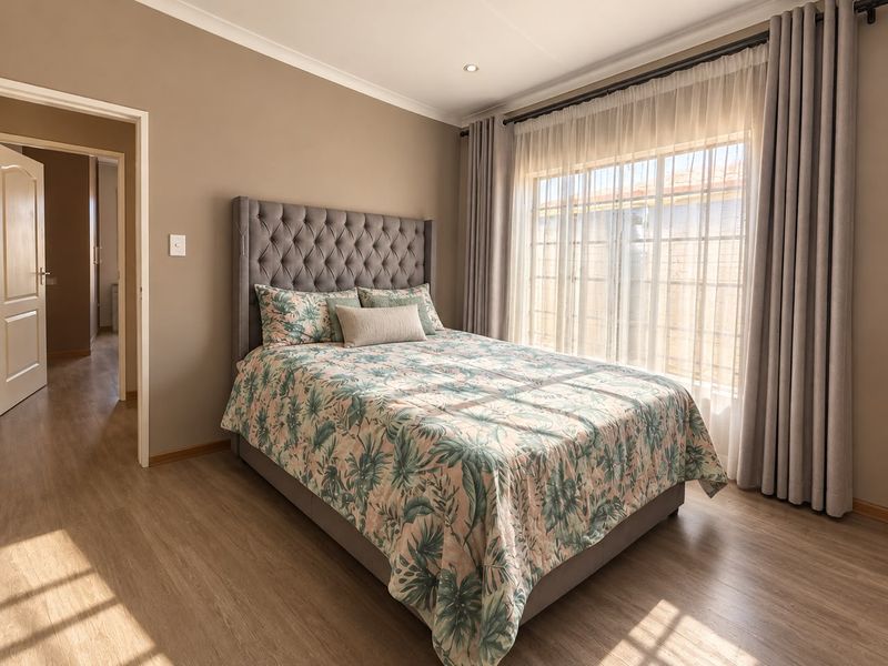 A well-maintained bedroom featuring laminate flooring, neutral wall tones, and natural light through large windows with integrated curtain tracks.