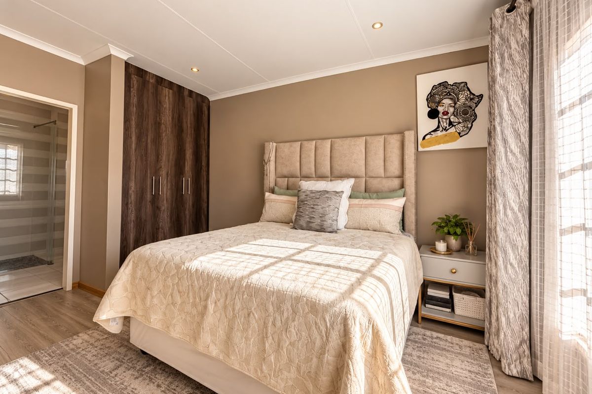 A well-maintained bedroom featuring built-in cupboards, recessed downlights, and laminate flooring, with convenient access to an en-suite bathroom.