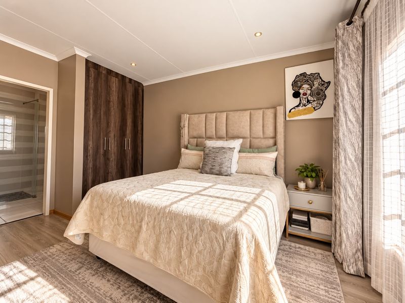 A well-maintained bedroom featuring built-in cupboards, recessed downlights, and laminate flooring, with convenient access to an en-suite bathroom.