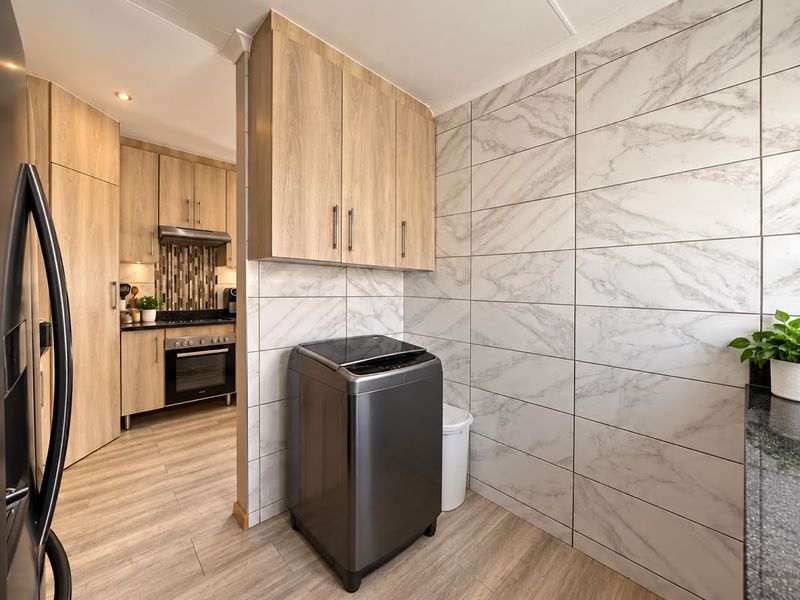 A modern, well-appointed scullery featuring marble-look wall tiling, ample built-in cabinetry, and durable laminate flooring, seamlessly connected to the main kitchen area.